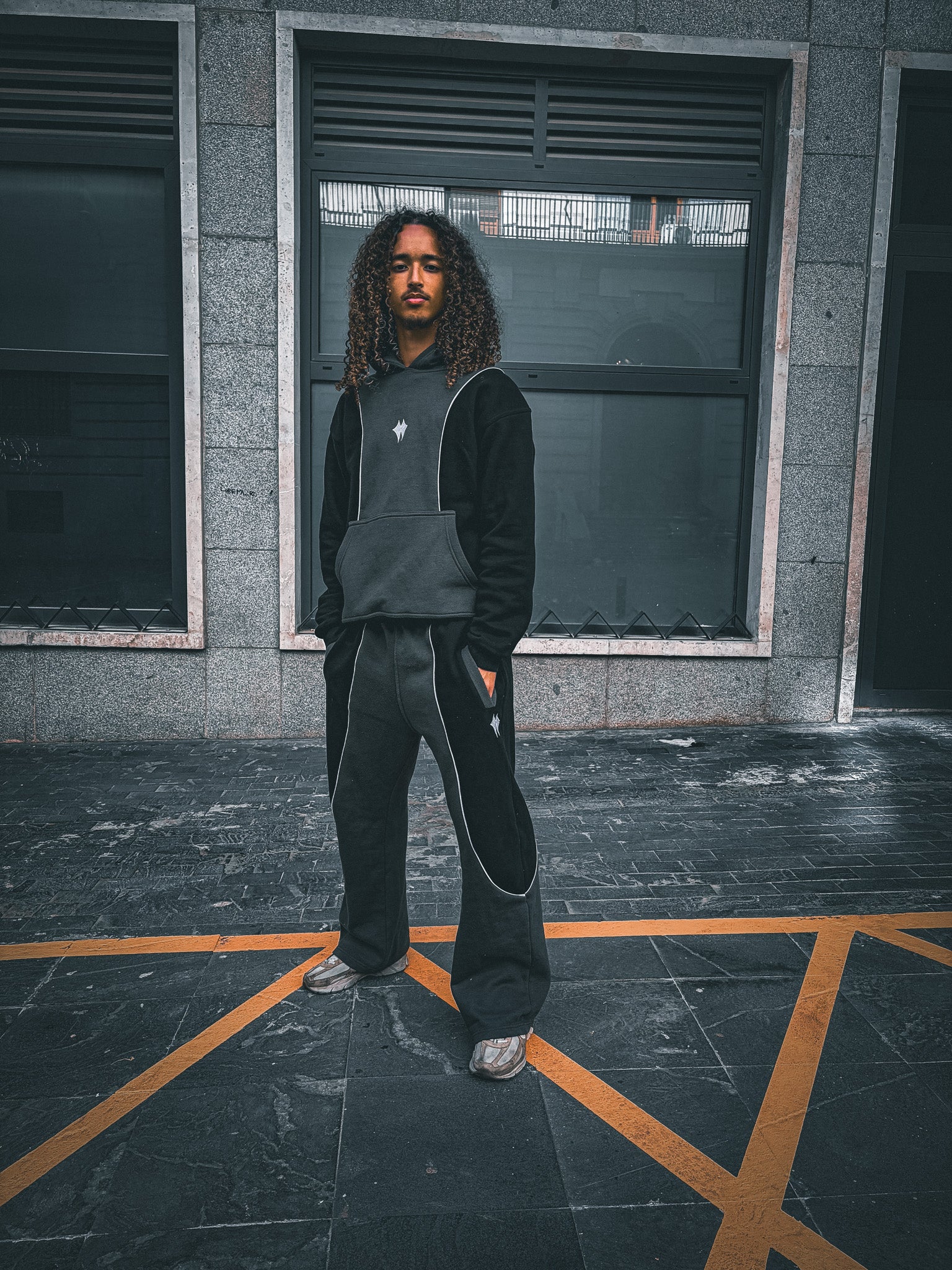 Model wearing a black and grey hooded top and matching wide-leg trousers in an Auwra street shoot